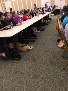 Guide dogs nap under long tables as their partners listen to a lecture.